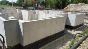 Betonnen funderingsmuren van een kelder die gedeeltelijk zijn behandeld met vloeibaar rubber om de kelder dicht te maken, omringd door uitgegraven aarde.